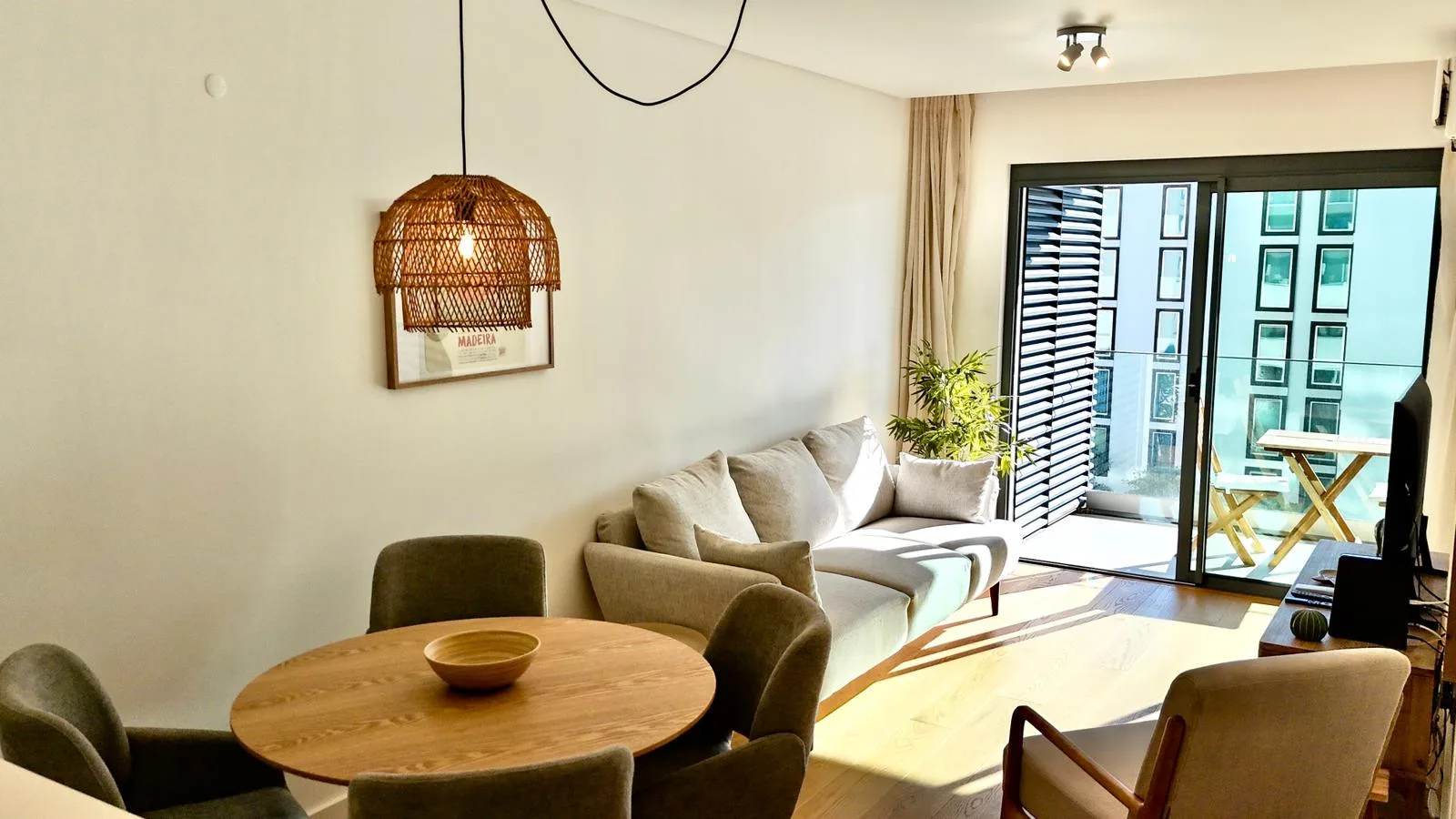 Una sala luminosa con asientos, una mesa redonda y puertas de vidrio hacia un balcón.