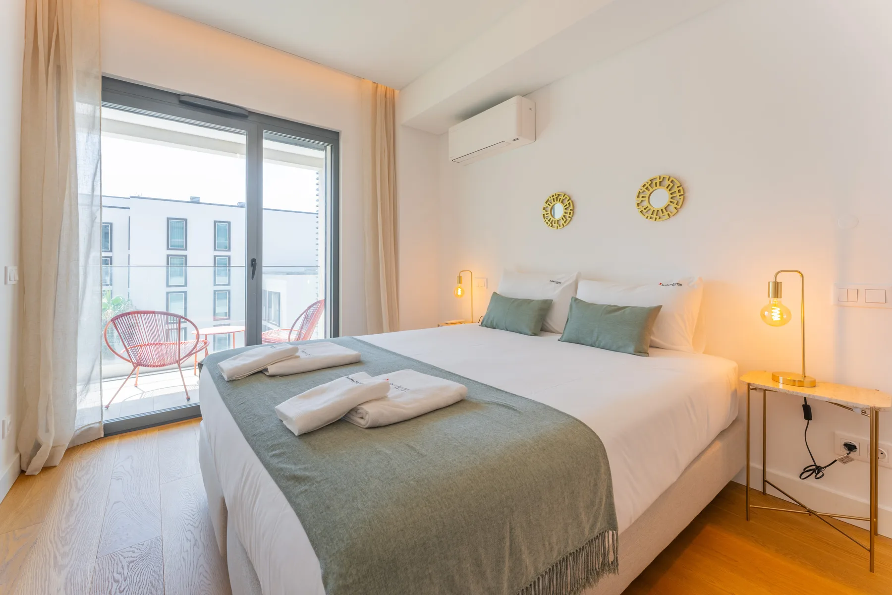 Un dormitorio luminoso con una cama grande, mesitas de noche y una puerta acristalada al balcón.