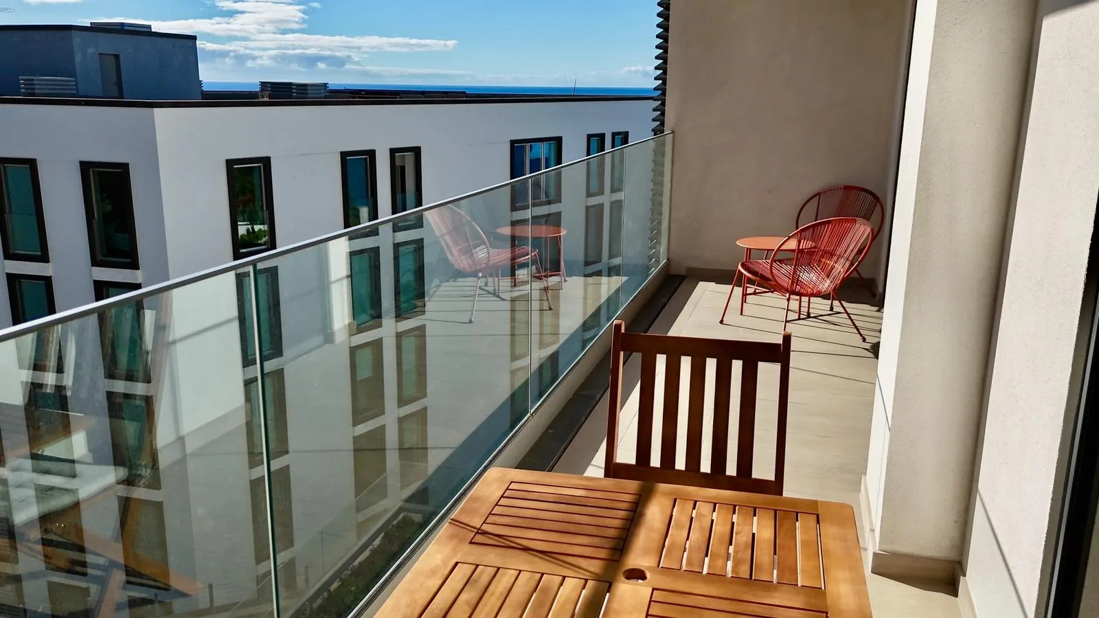 Un balcón con una mesa de madera y asientos da a un edificio vecino.