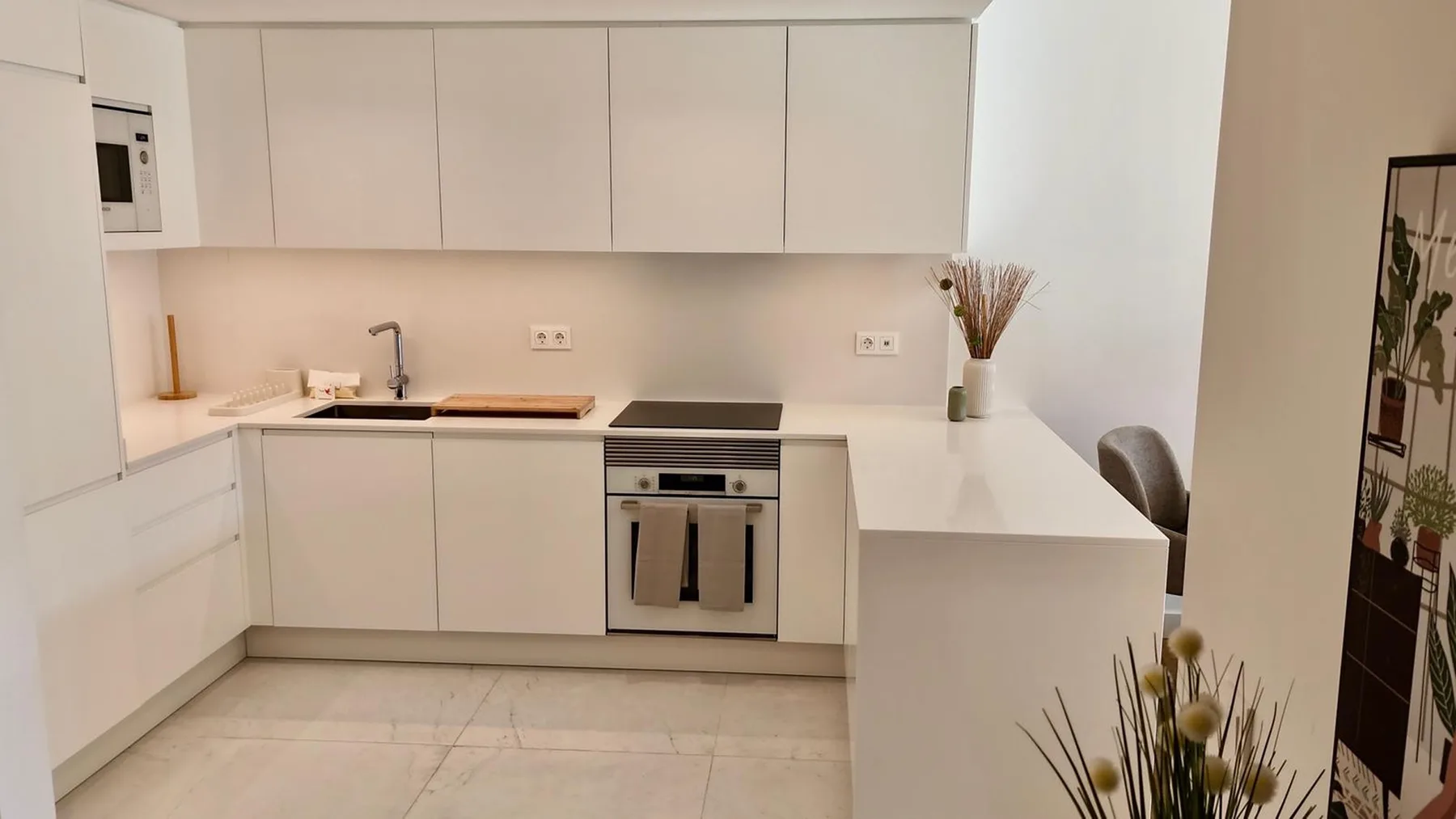 Una cocina moderna y luminosa con armarios blancos, una placa de cocina y una barra.