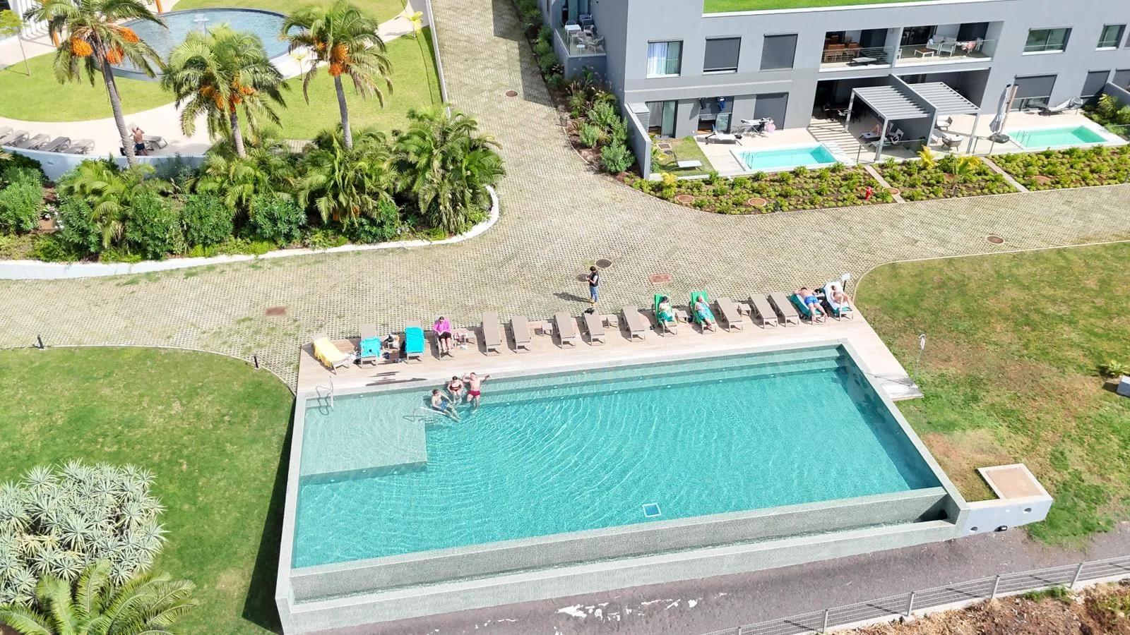 Una piscina al aire libre está rodeada de tumbonas, césped y zonas ajardinadas.