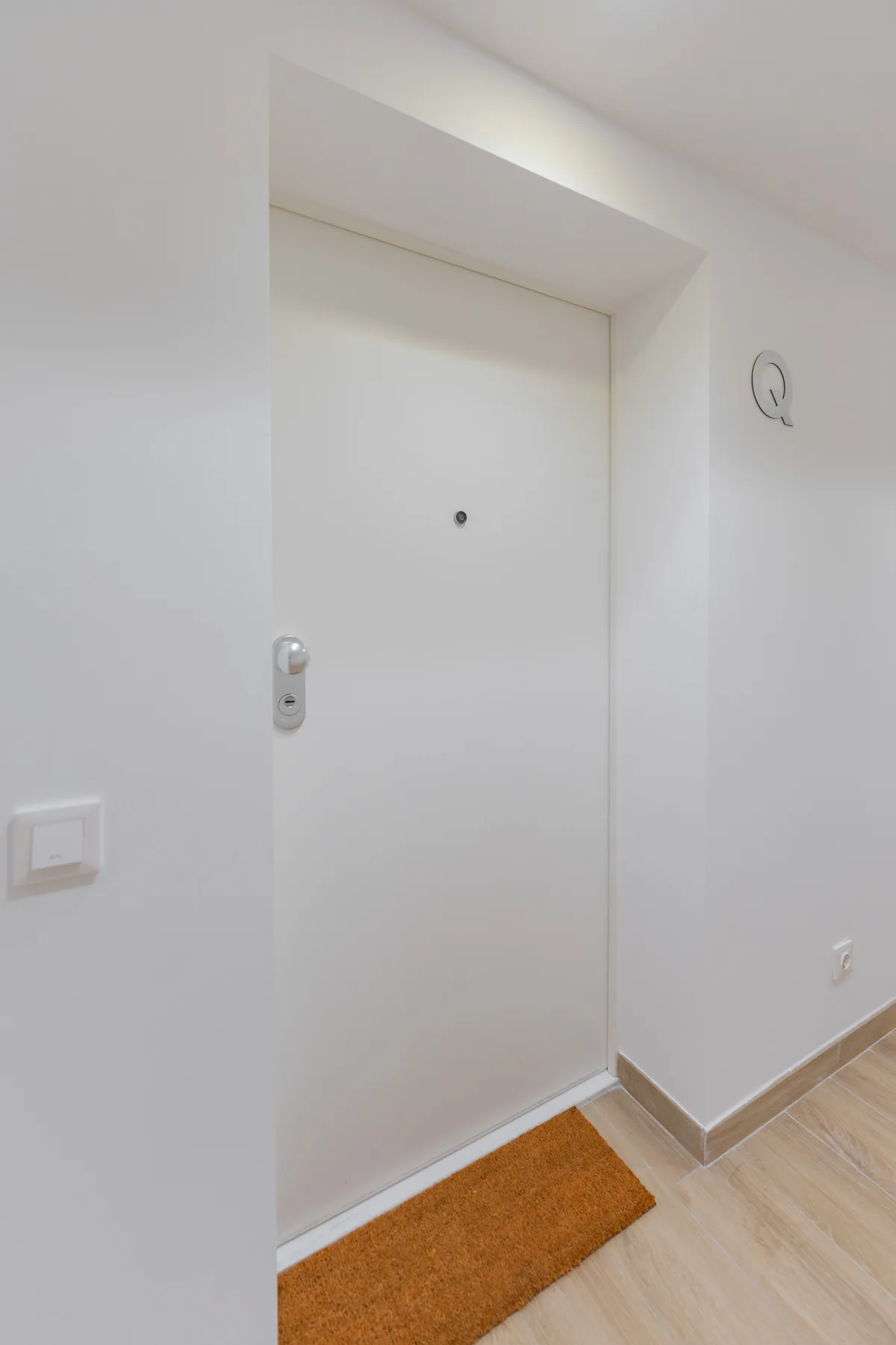Una puerta blanca da a un pasillo claro con un felpudo.