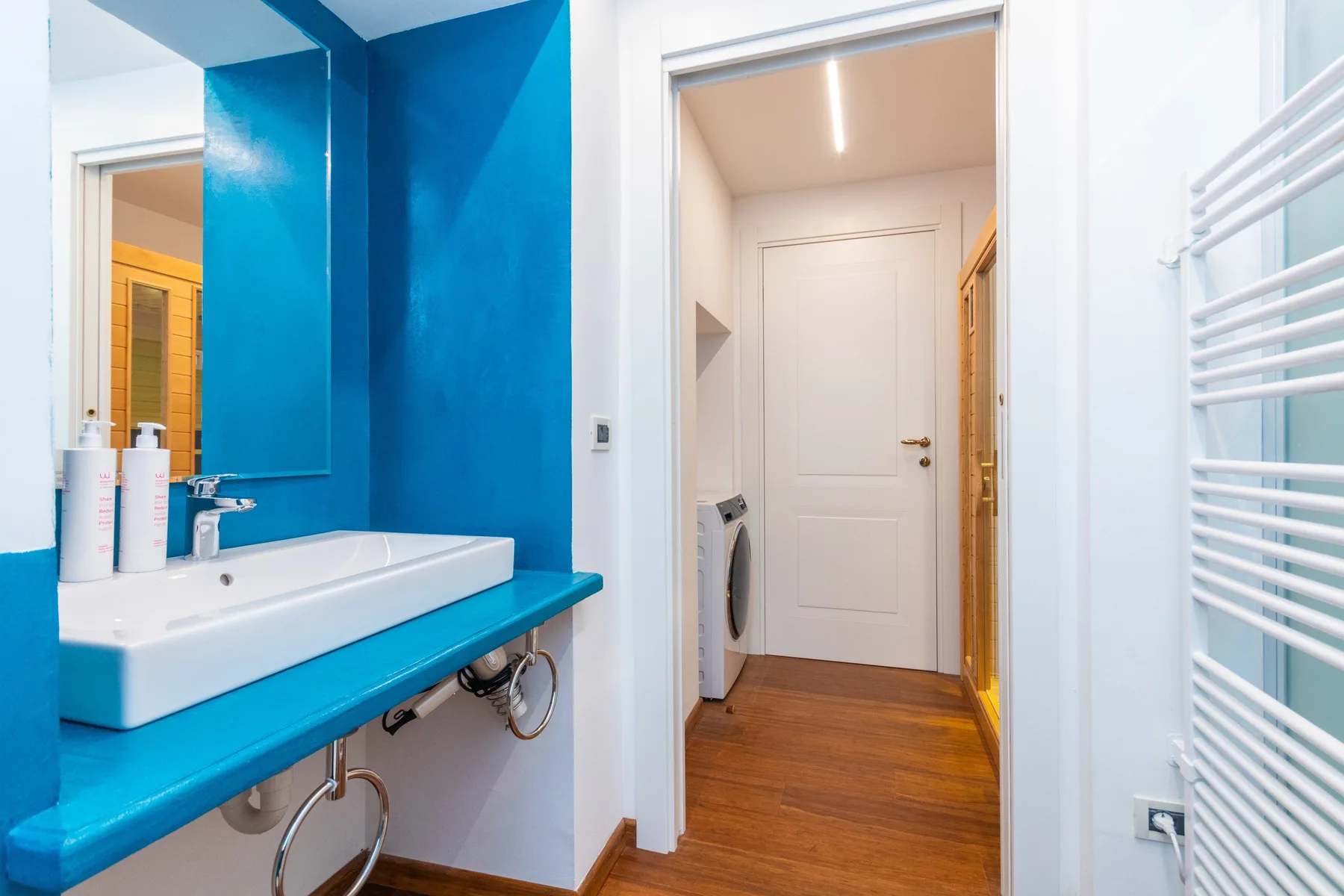 A bathroom sink and mirror open onto a hallway with a closed door.