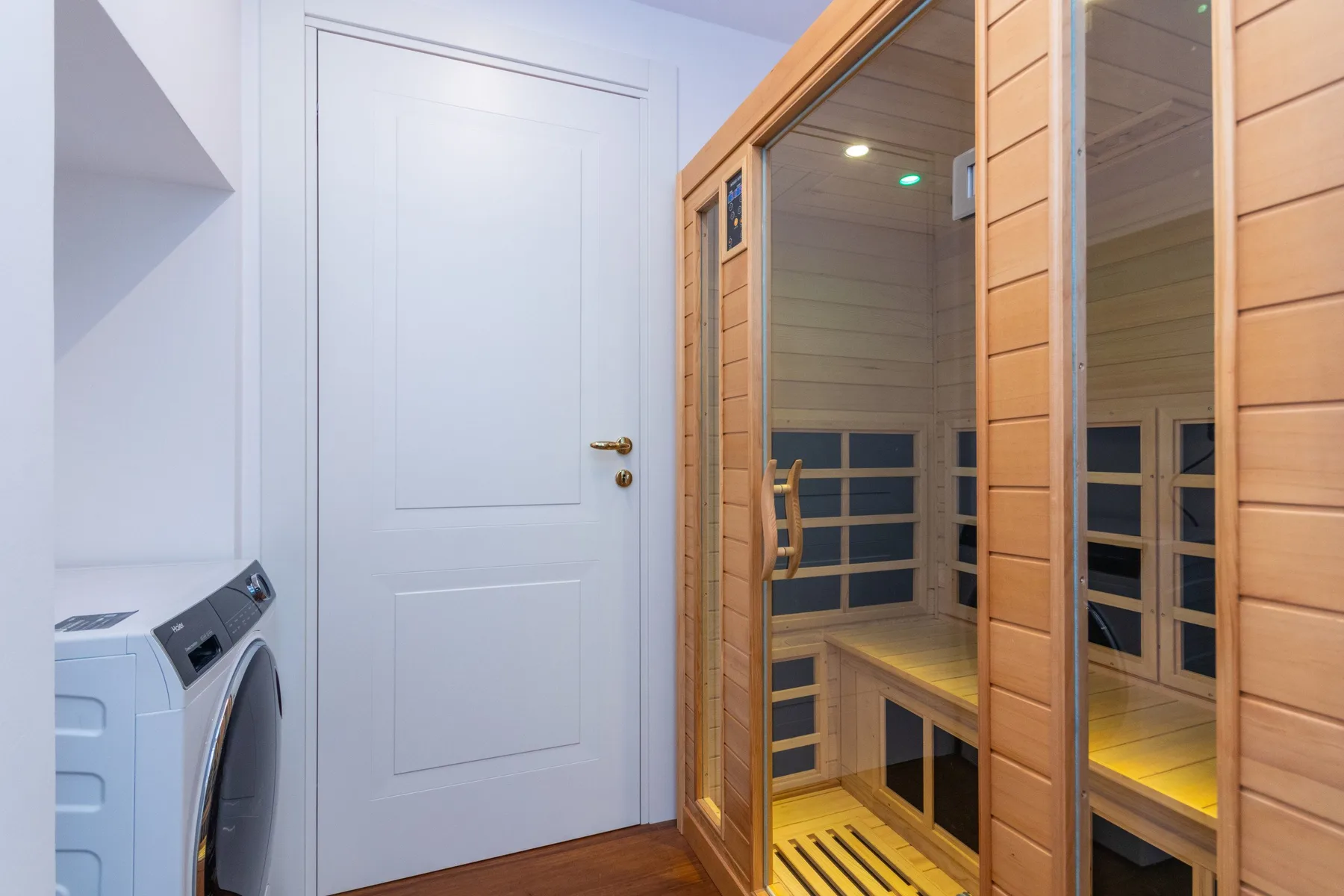 A wood-paneled sauna with glass doors stands beside a white interior door.