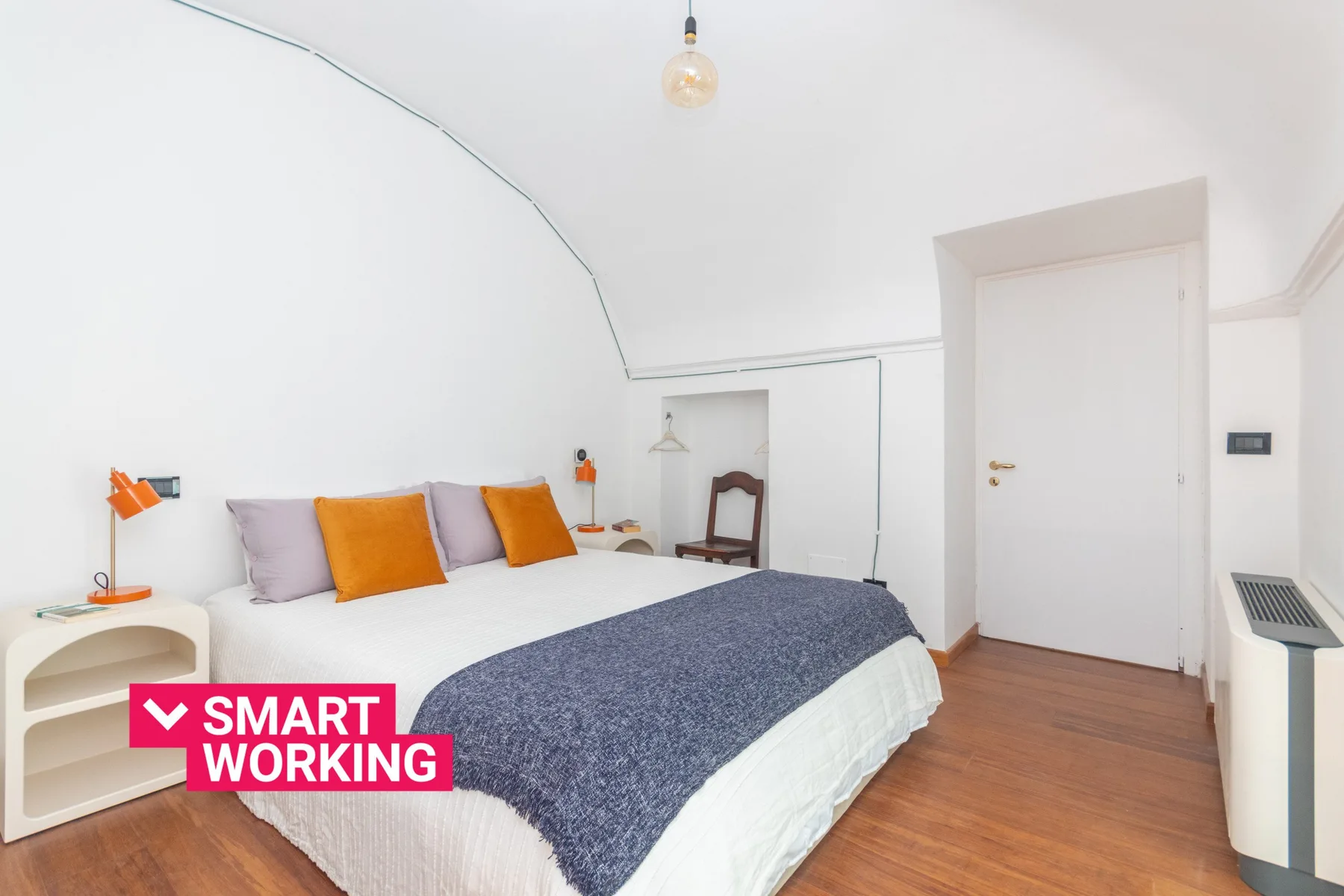 Un dormitorio luminoso con una cama, almohadas de colores y suelo de madera.