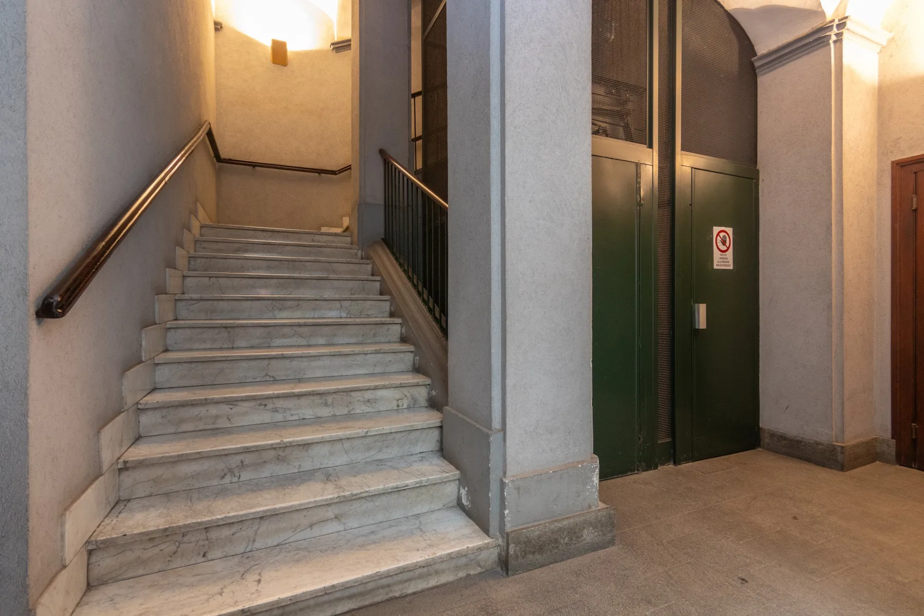 An indoor stairwell with marble steps and a dark green elevator door.