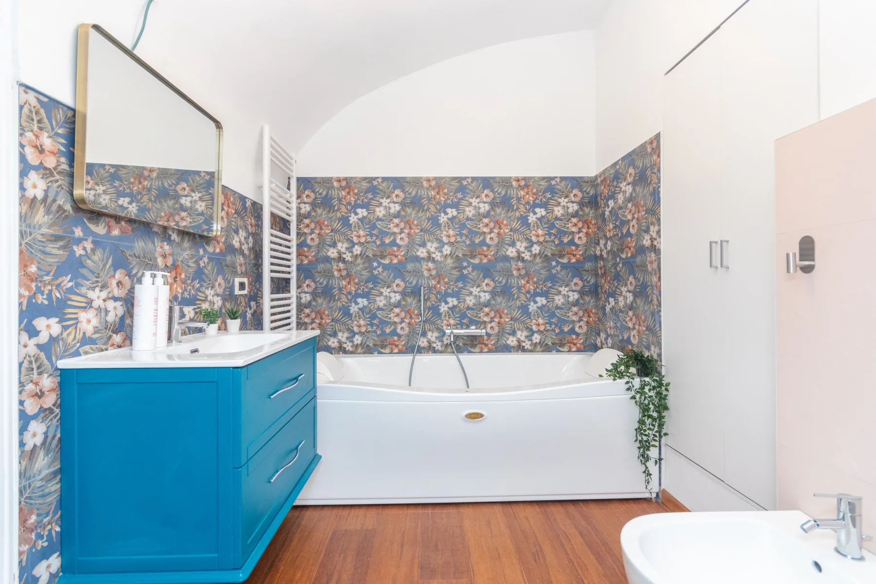 A bathroom with a bathtub, blue vanity, and floral patterned walls.