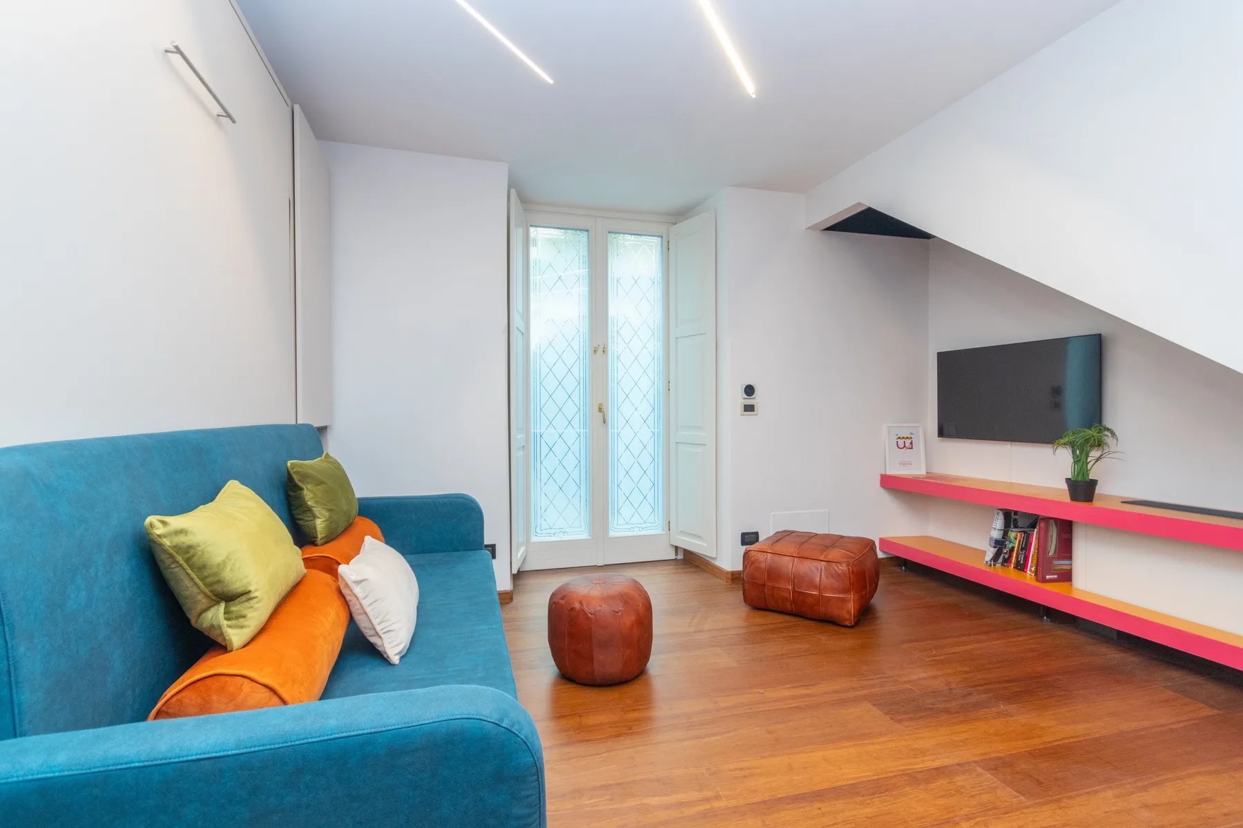 A bright living room with colorful seating, a television, and tall glazed doors.