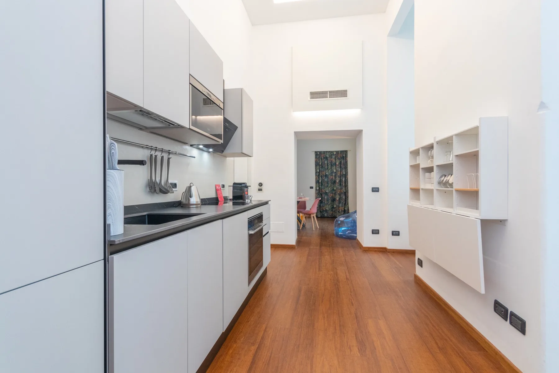 A modern kitchen with white cabinetry, a dark countertop, and wood flooring.