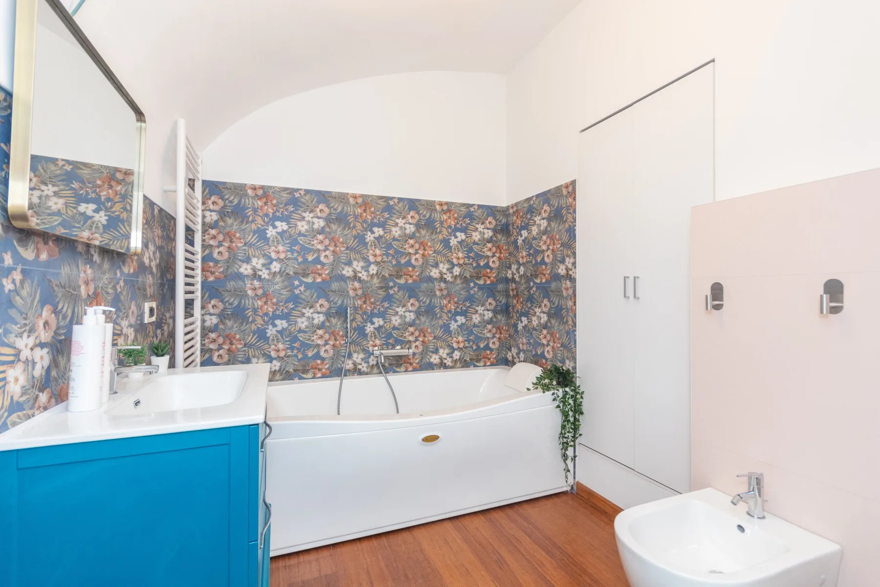 A bathroom with a bathtub, sink, and colorful floral wall covering.