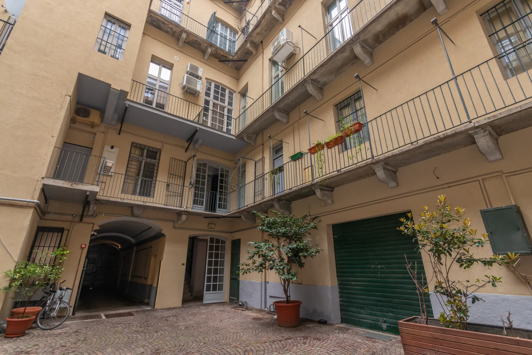 An enclosed courtyard with balconies, potted plants, and a paved ground.