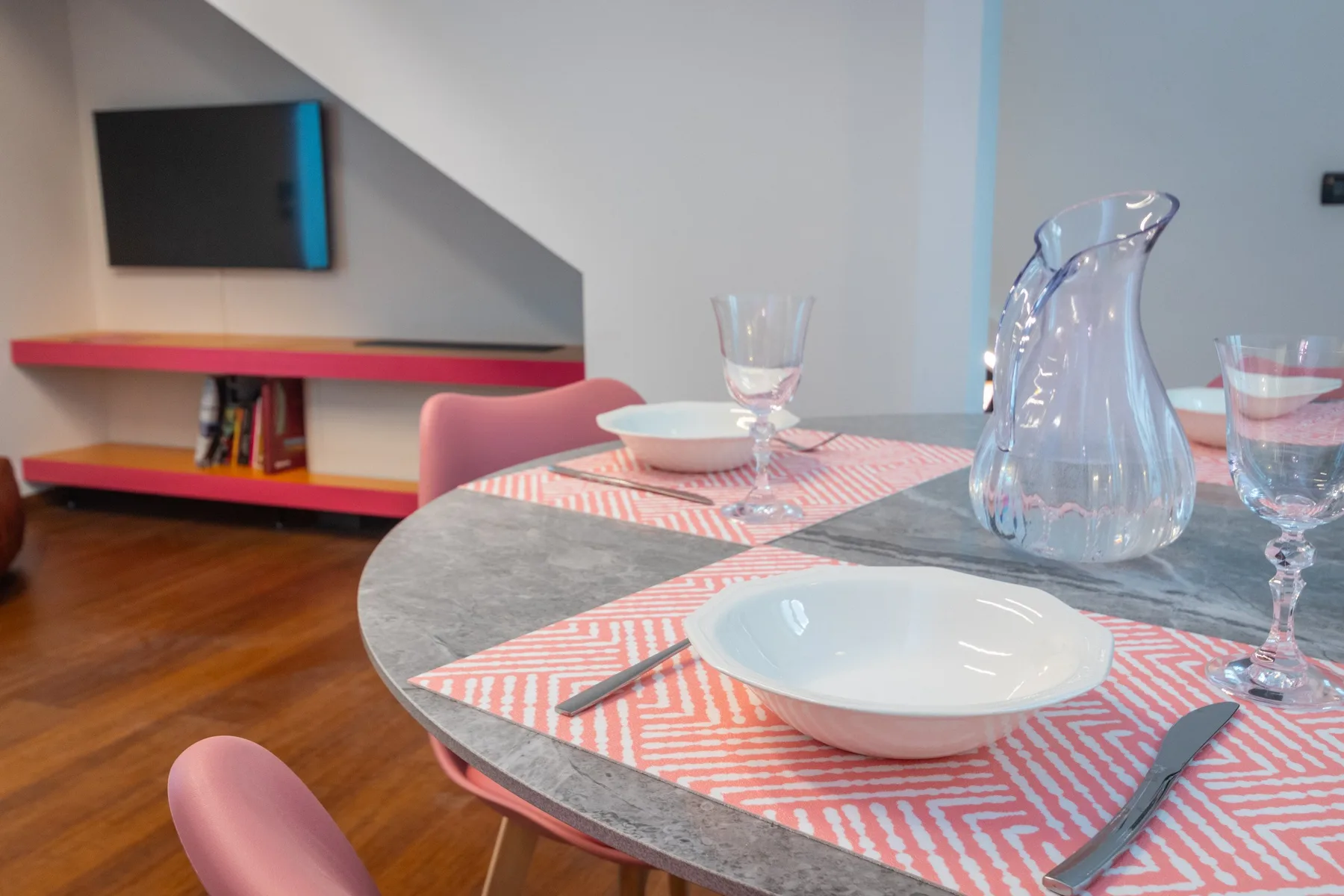 A dining table is set with plates, glasses, and a glass pitcher.