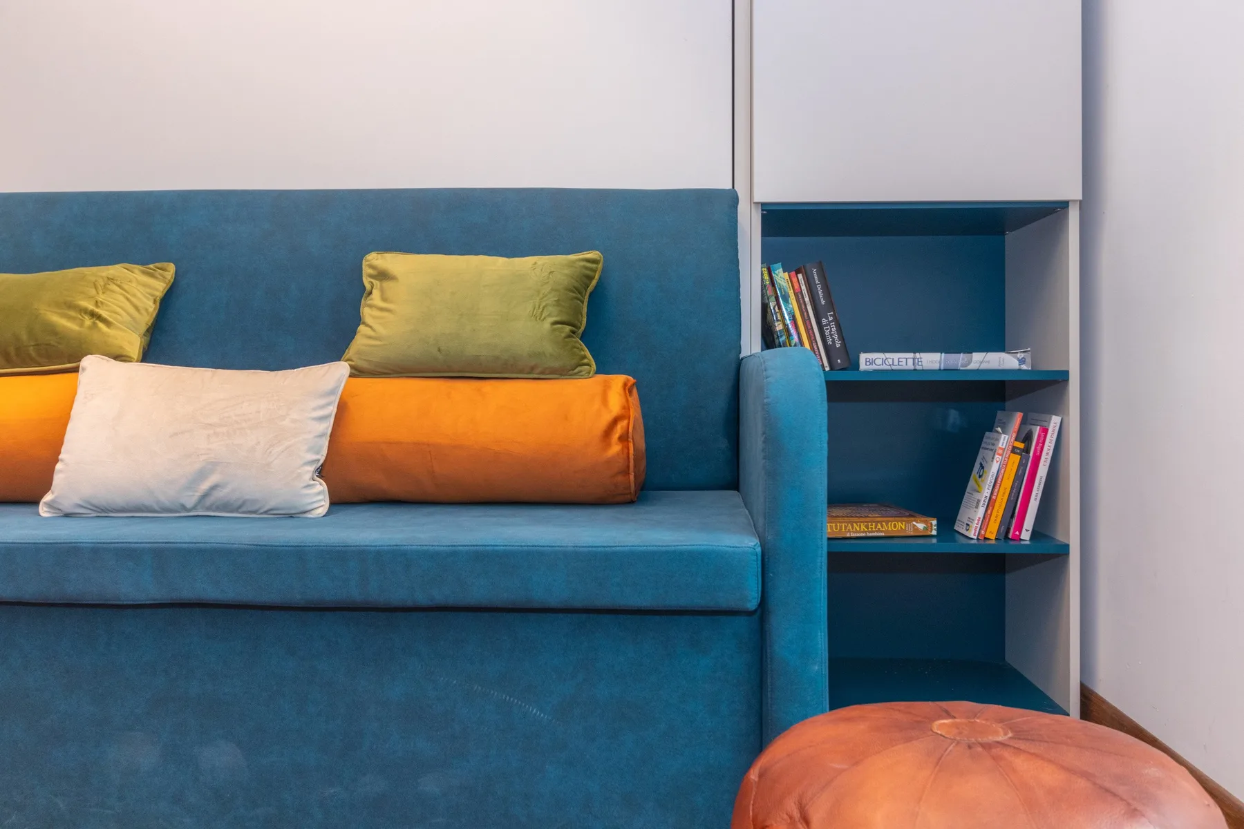 A blue sofa sits beside a built-in bookshelf with colorful books.