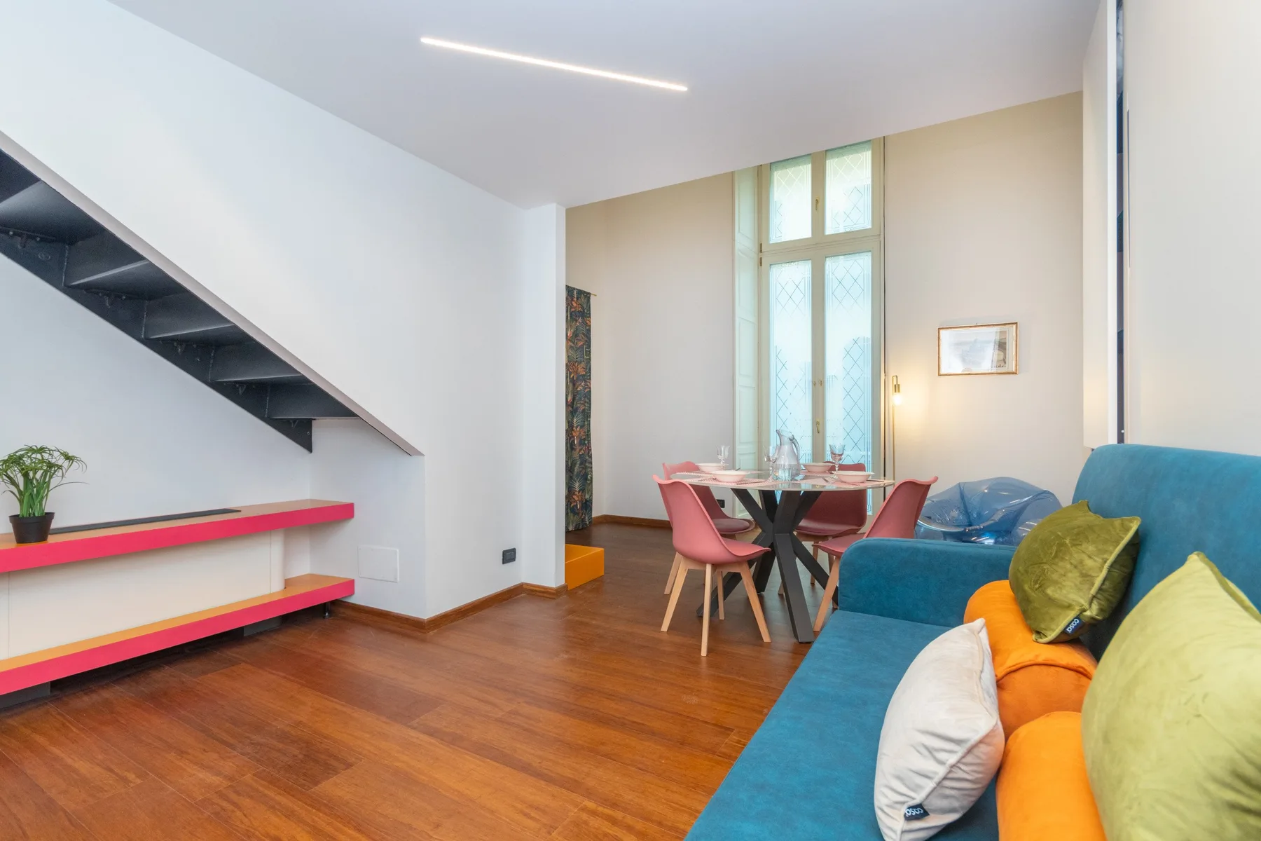 A living and dining area with colorful seating and a tall window.