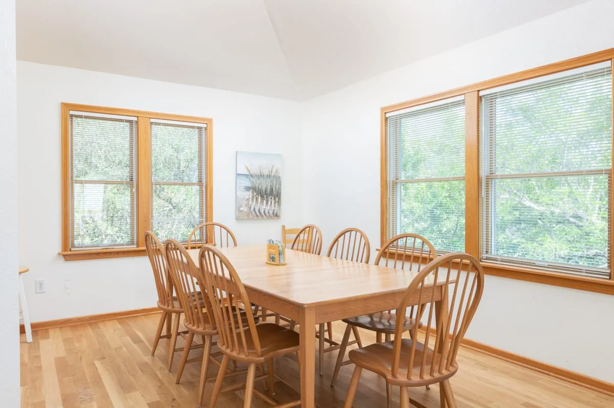 Un comedor con una mesa de madera y sillas junto a grandes ventanas.