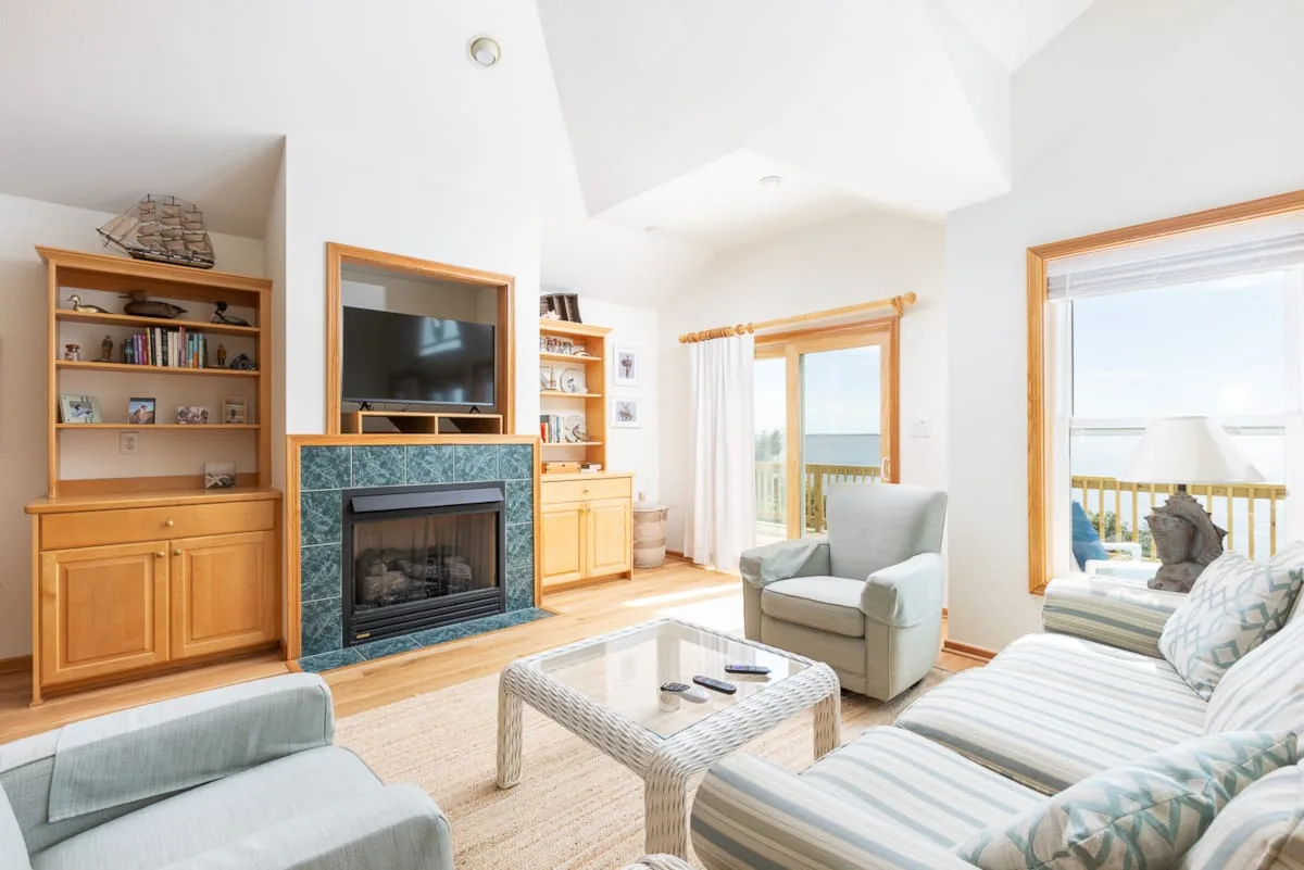 A bright living room with a fireplace, television, and seating beside large windows.