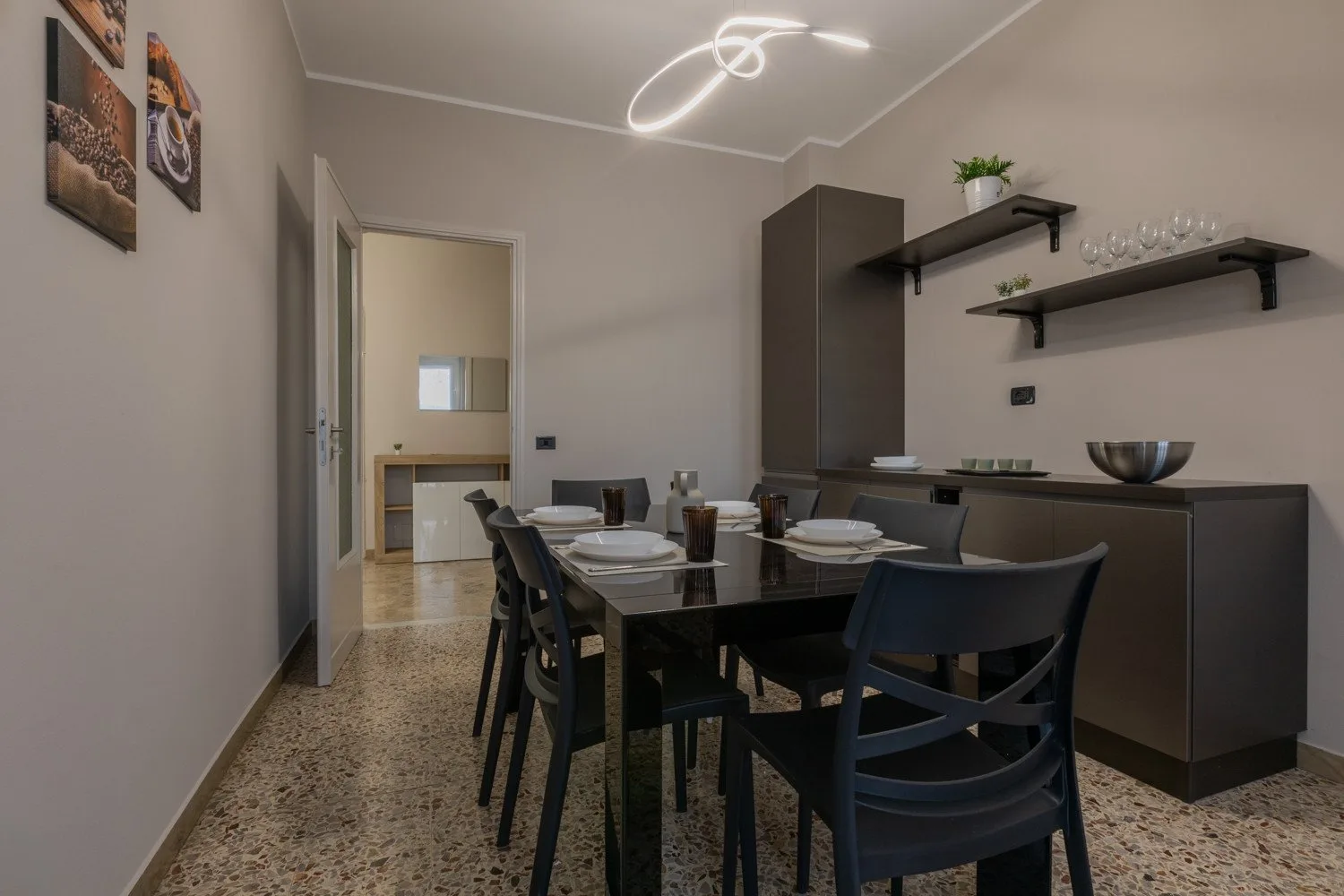 A dining area with a table set for a meal beside dark cabinets and wall shelves.