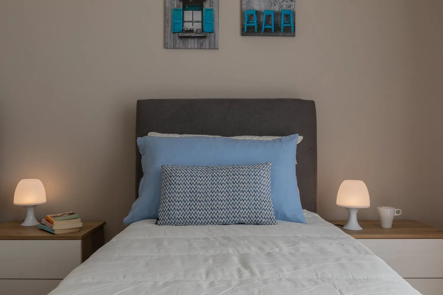 A neatly made bed with blue pillows sits against a plain wall.