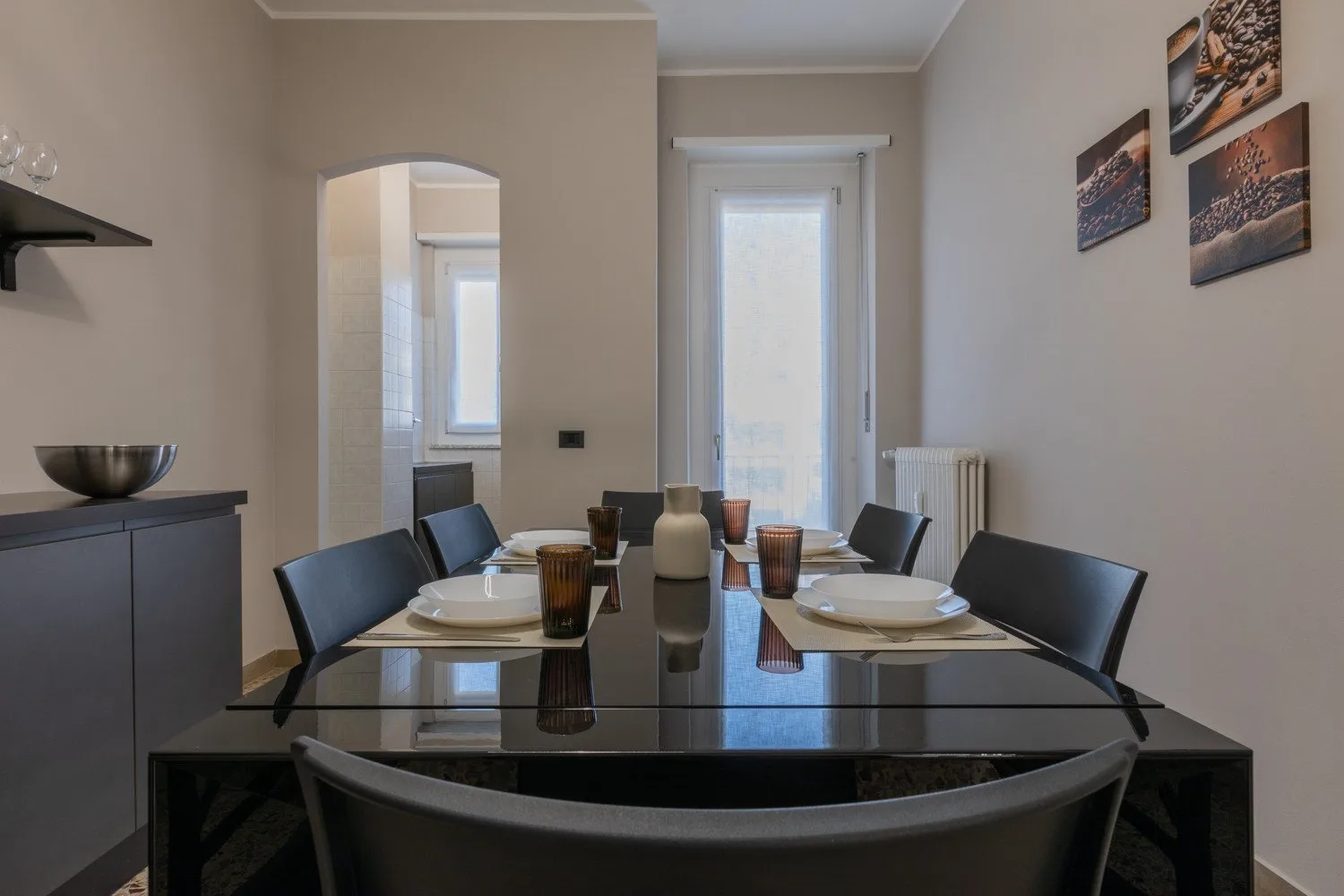 A dining area with a glass table and chairs beneath framed wall art.