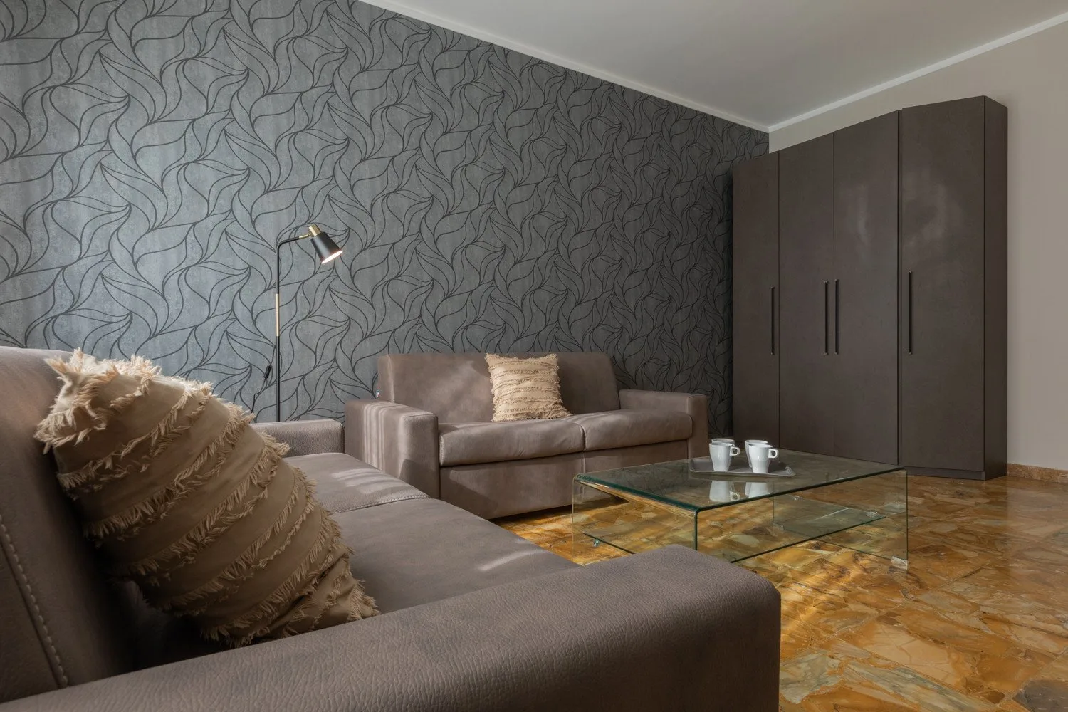 A living room with upholstered seating, a glass coffee table, and a tall wardrobe.