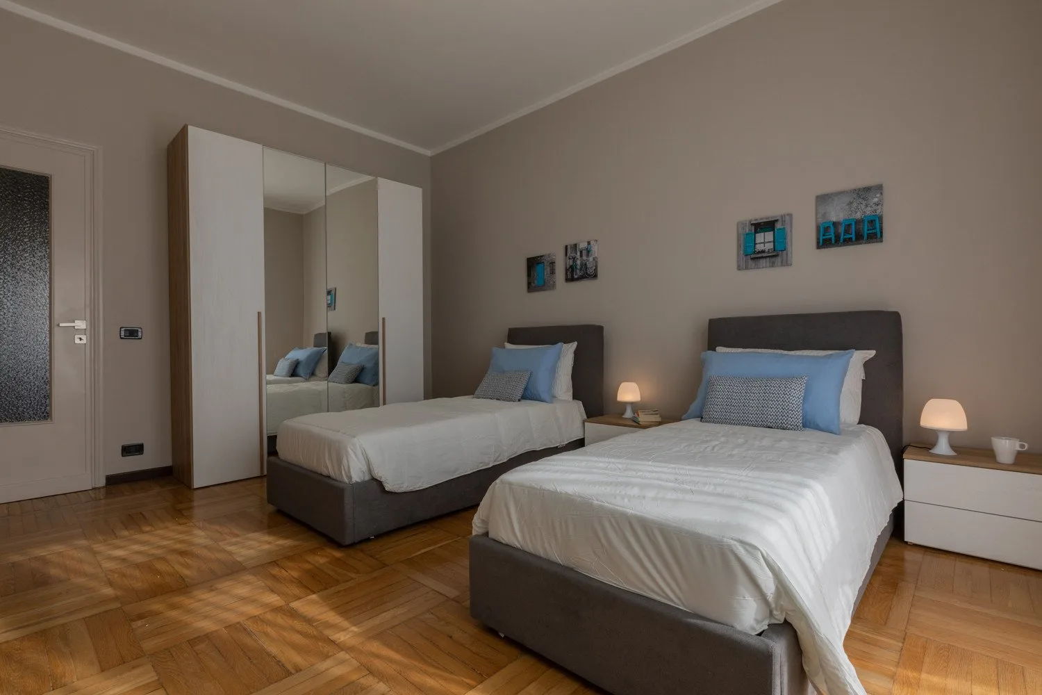 A bedroom with two beds, mirrored wardrobes, and framed wall art.