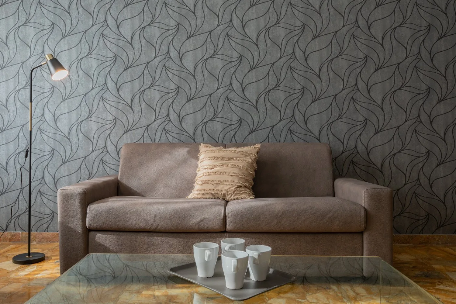 A living room with a brown sofa, patterned wallpaper, and a glass coffee table.