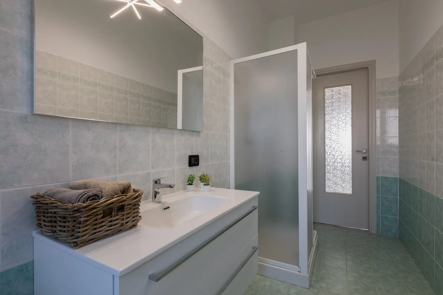 A tiled bathroom with a sink vanity, mirror, and frosted-glass door.