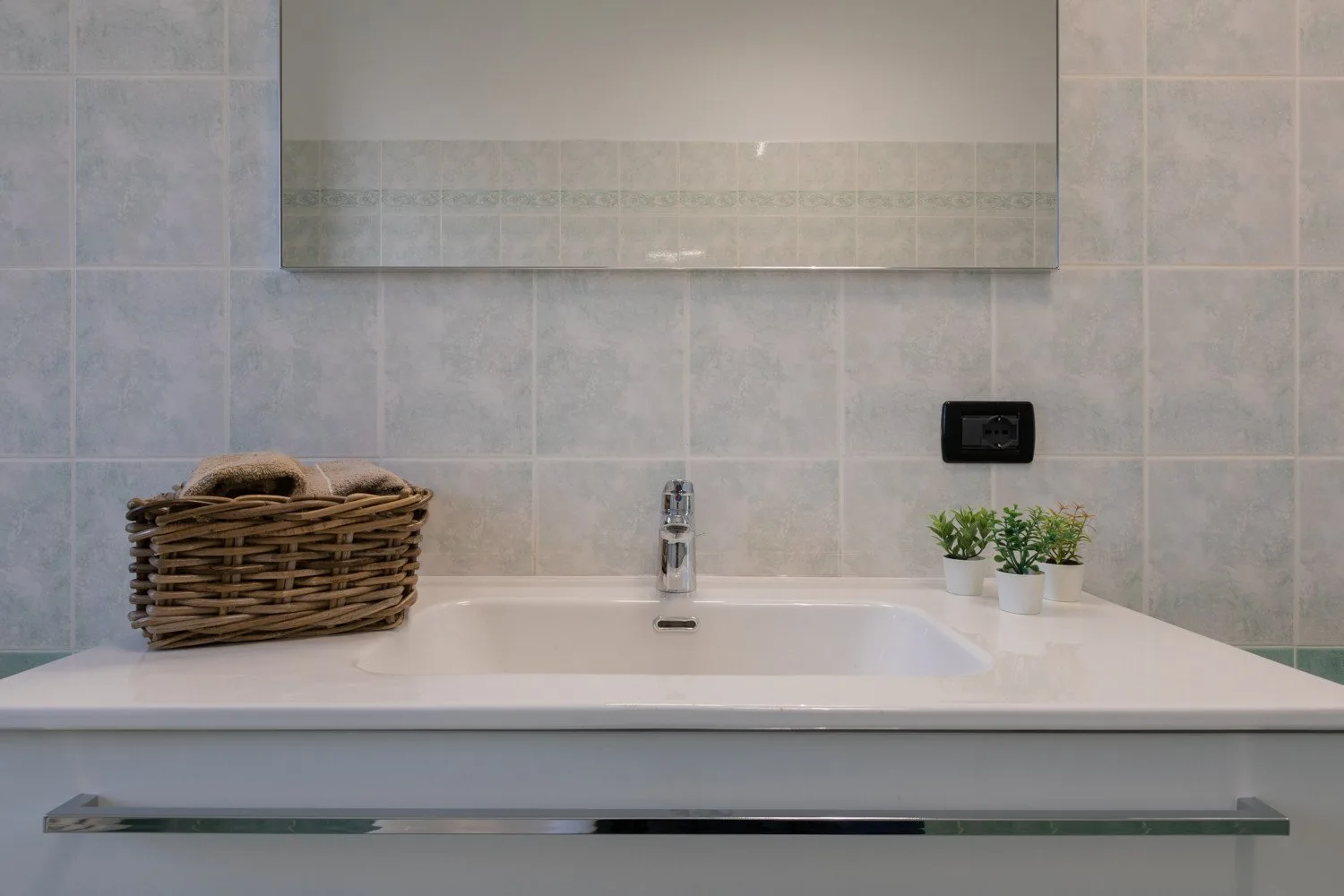A bathroom vanity with a sink, mirror, and small potted plants.