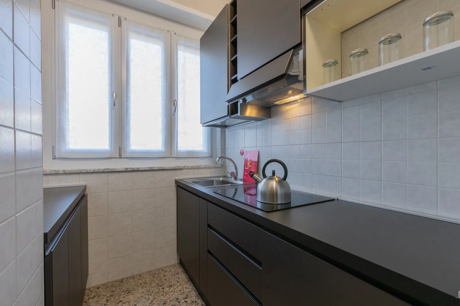 A compact kitchen with dark cabinets, a cooktop, and windows.