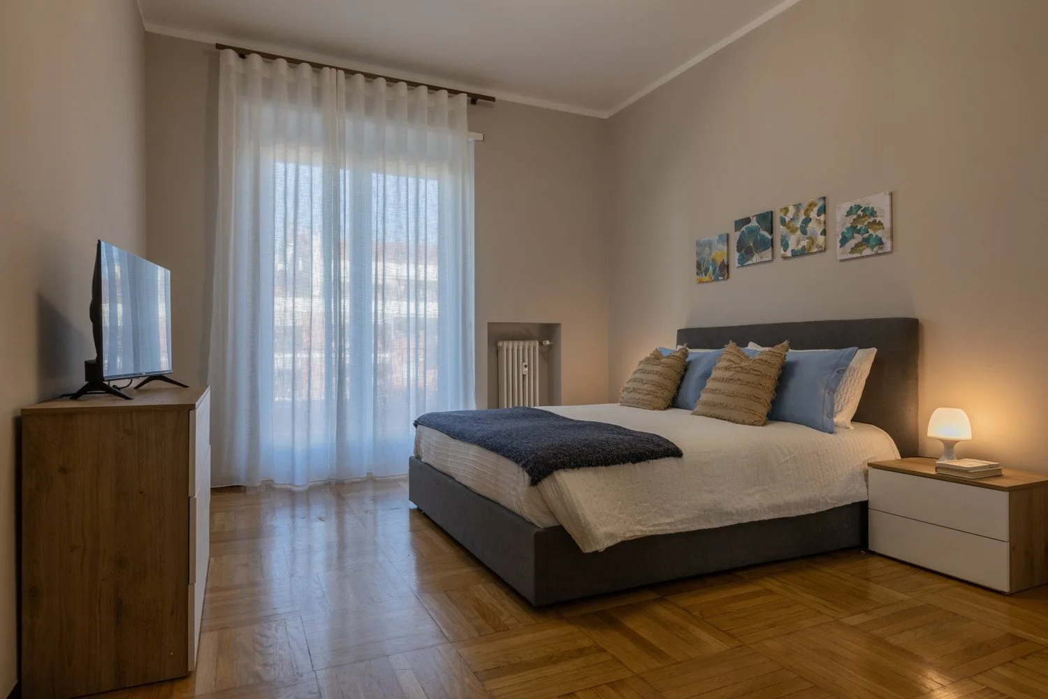 A bedroom with a bed, bedside table, and tall curtained window.