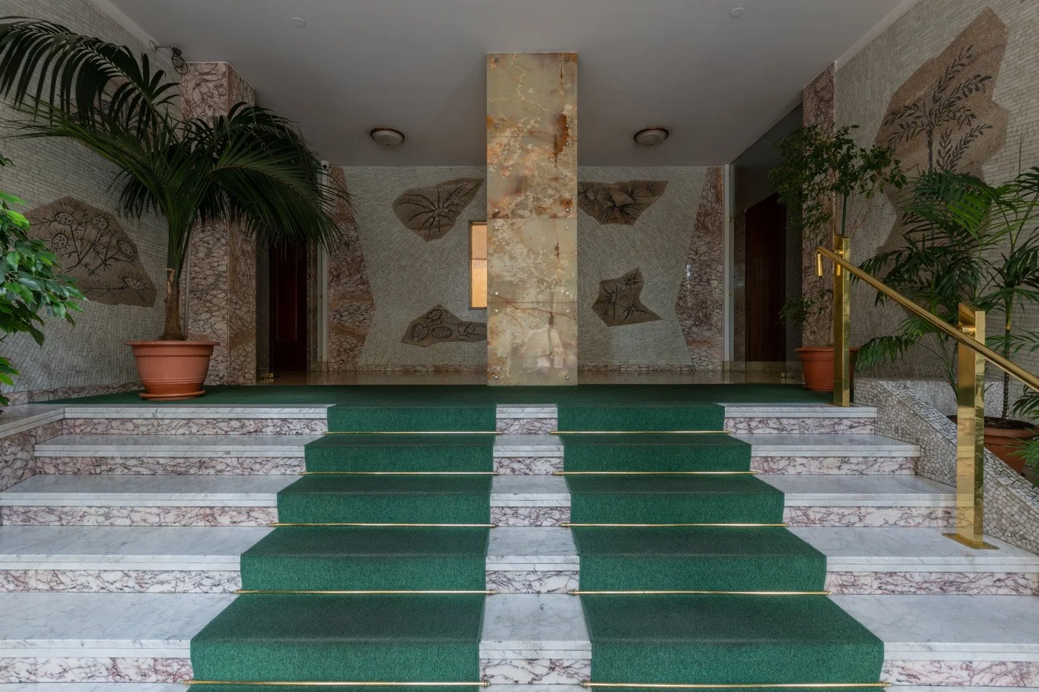 A tiled interior entrance features broad steps with green runners and potted plants.