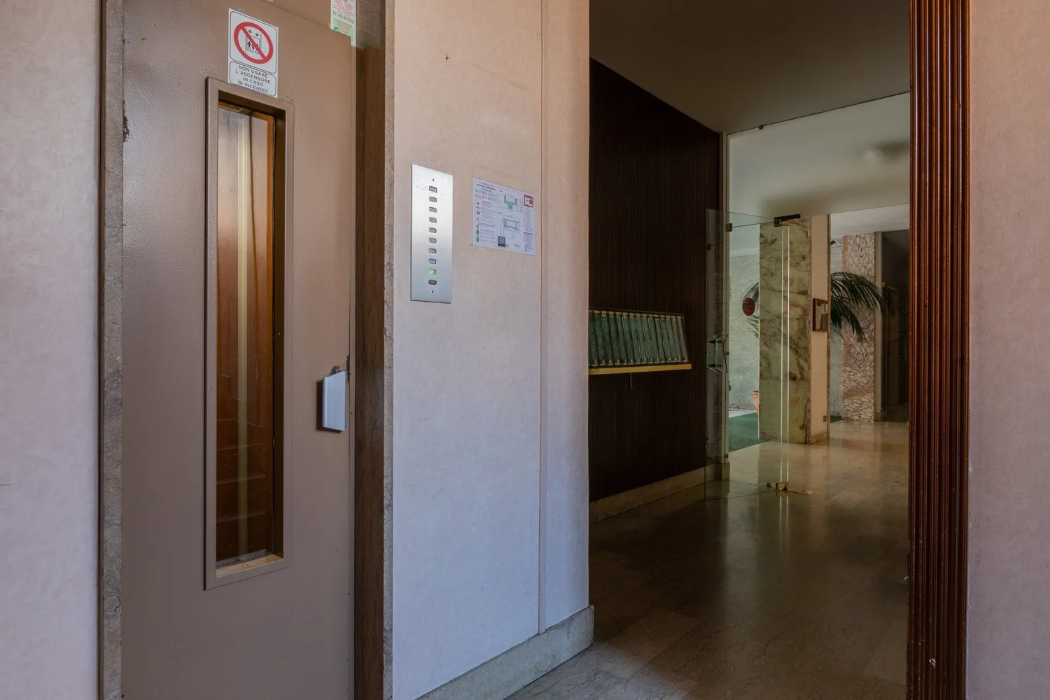 An elevator entrance opens onto an indoor hallway with polished flooring.