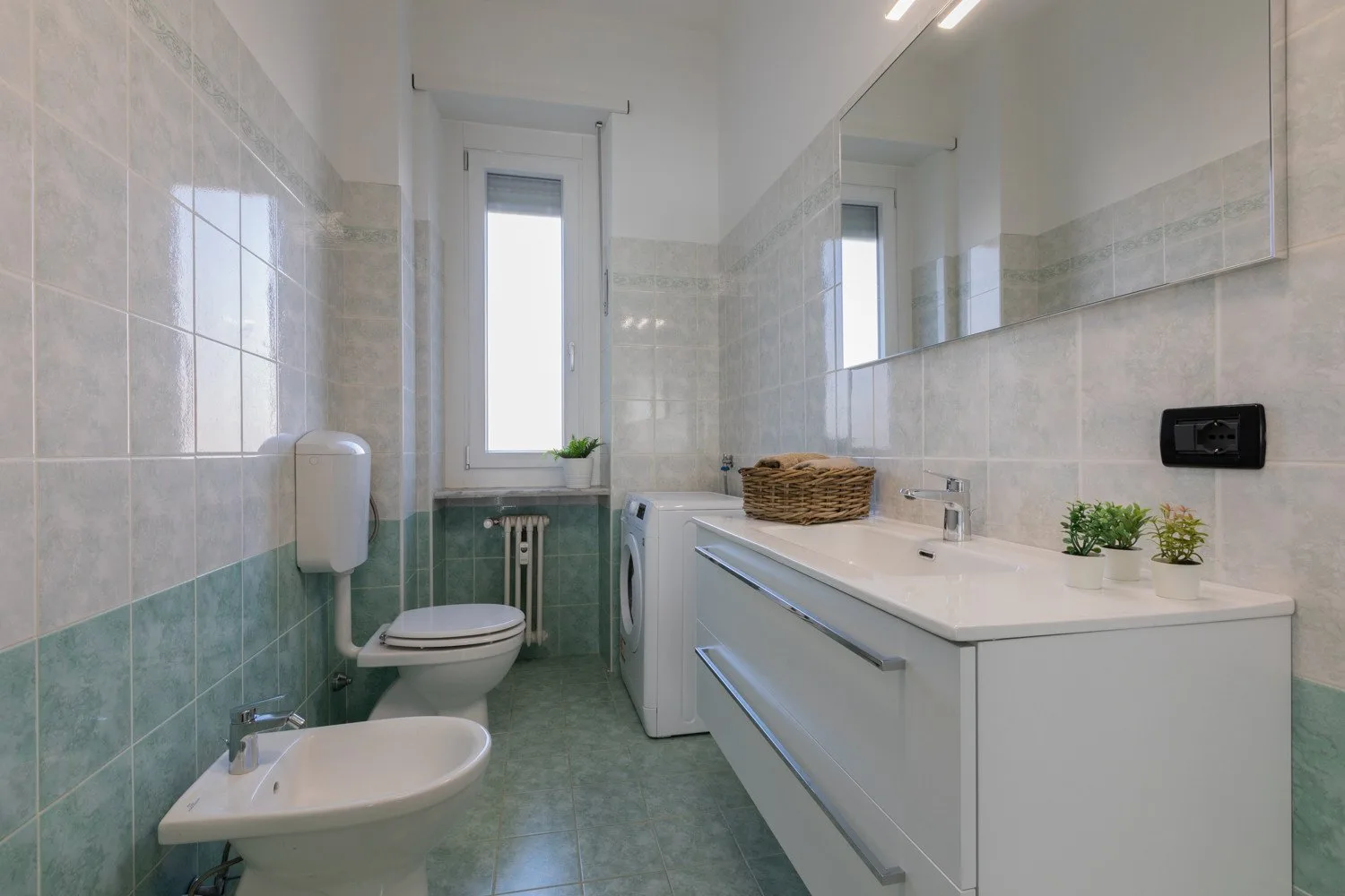 A tiled bathroom with a vanity, toilet, and window.