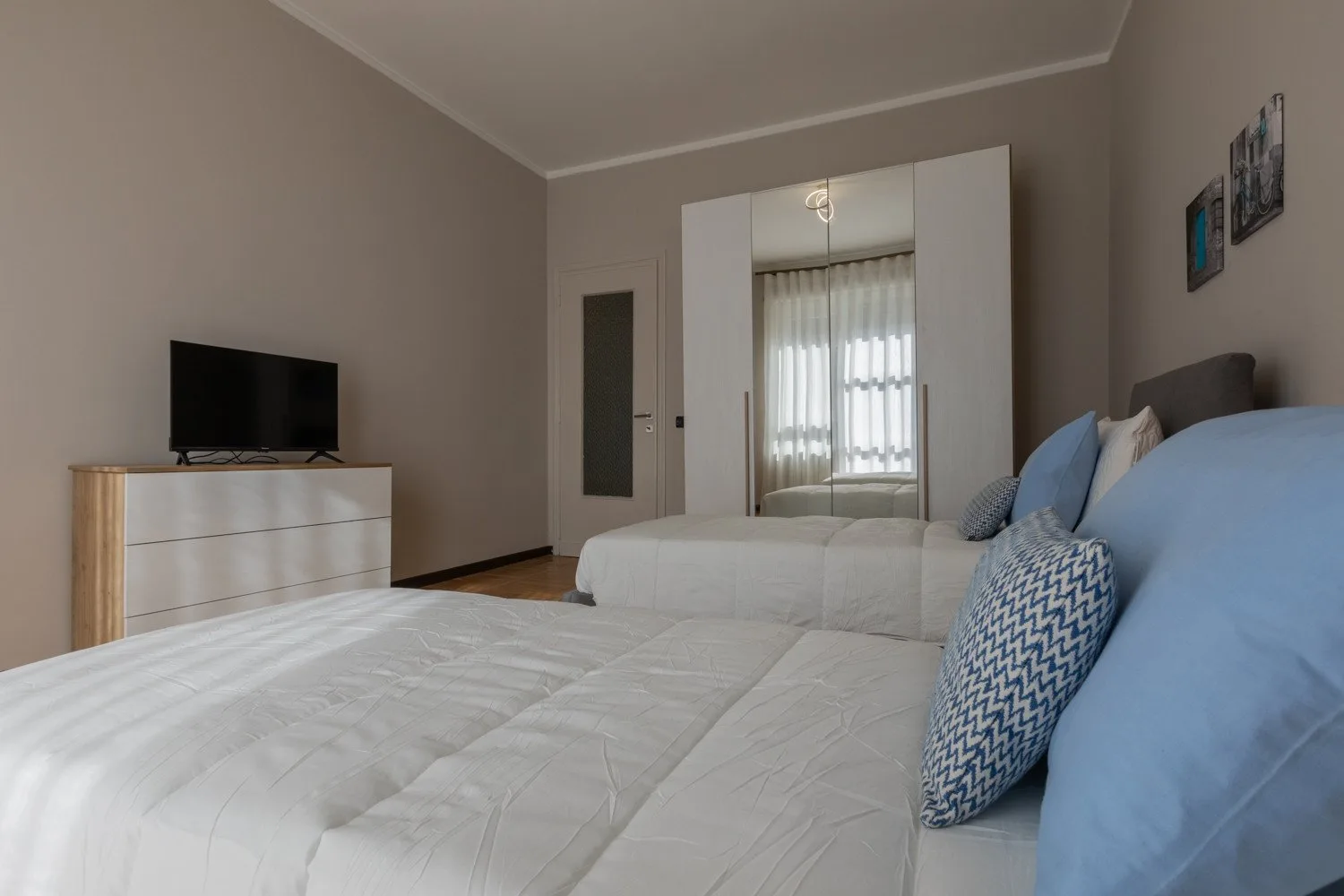 A bedroom with beds, a television, and a mirrored wardrobe.