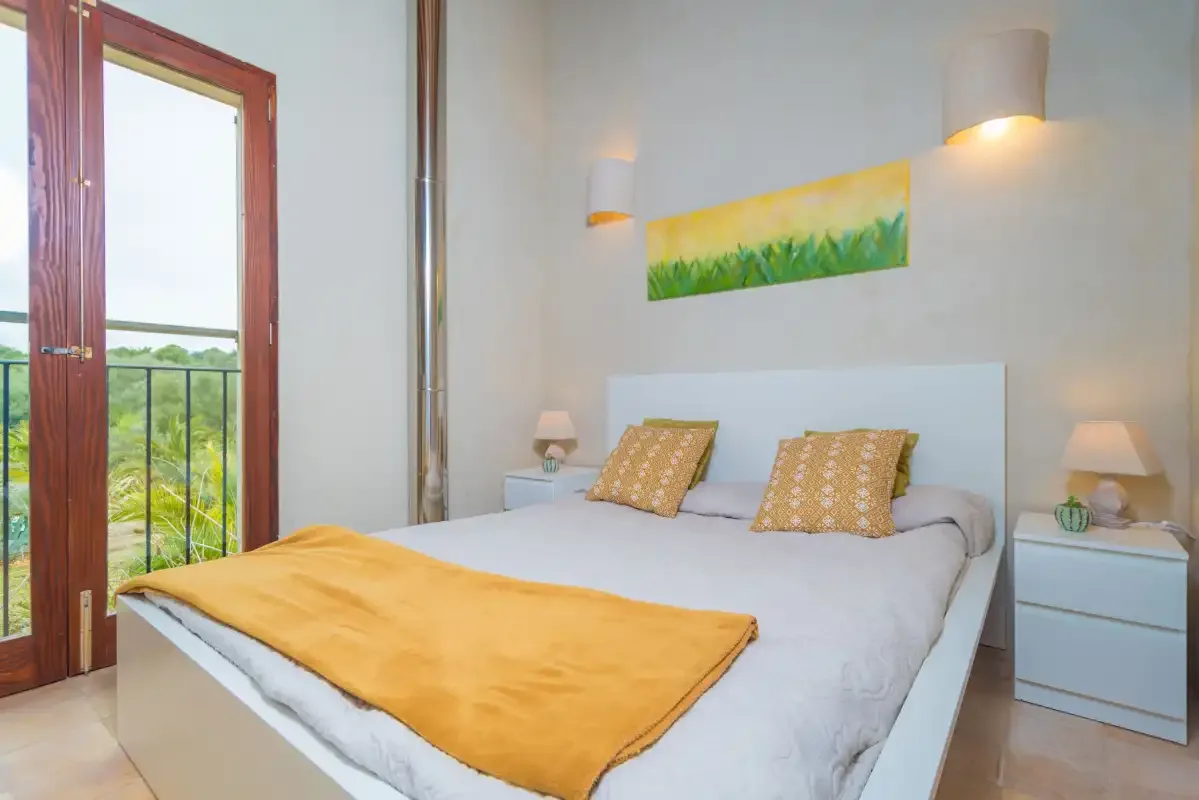 Un dormitorio con una cama, mesitas de noche y una puerta de cristal que da a un balcón.