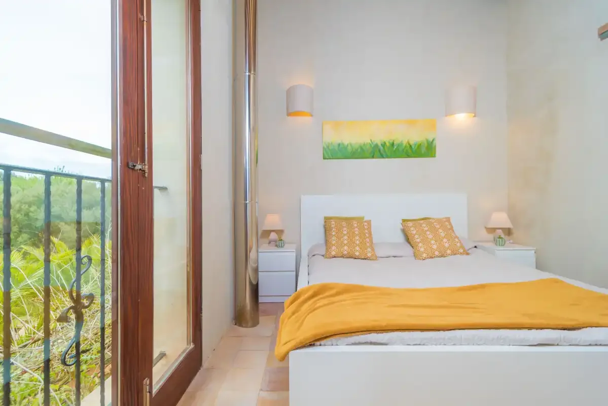 Un dormitorio con una cama doble, mesitas de noche y una puerta al balcón.