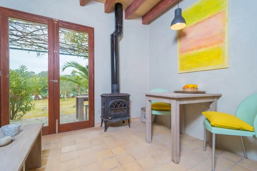 Un luminoso rincón de comedor tiene una mesa de madera, asientos coloridos y una estufa negra.