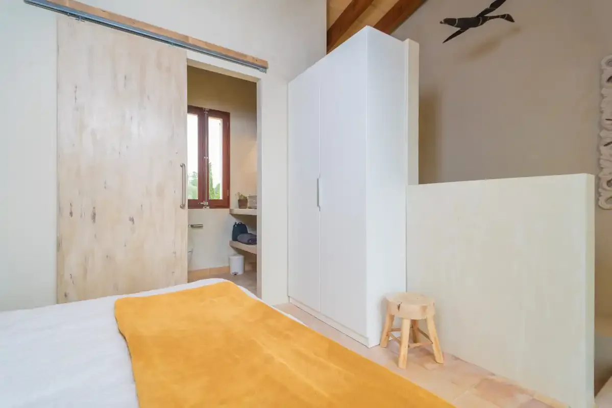 Un dormitorio con una cama, un armario blanco y un taburete de madera.
