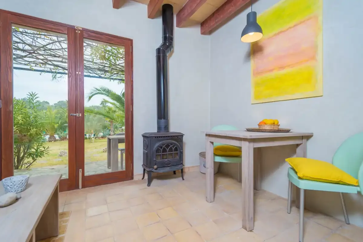 Un comedor luminoso con una mesa pequeña, asientos y una estufa de leña.