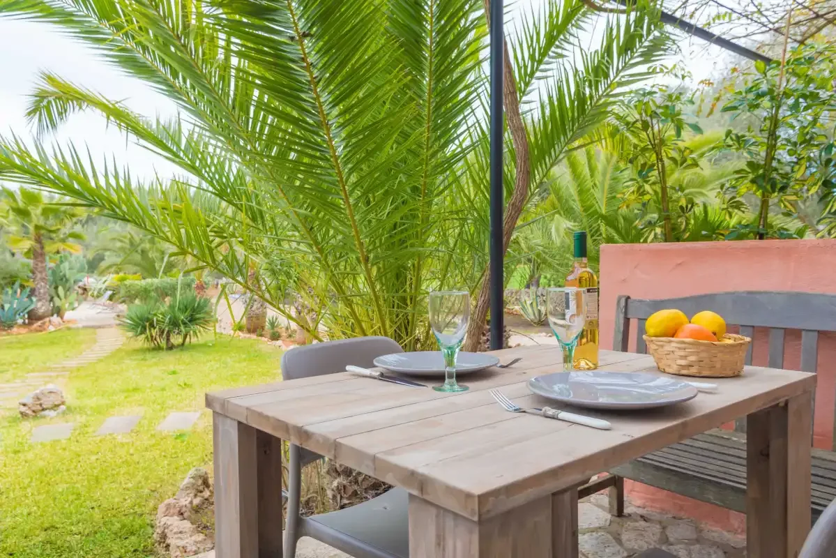 Mesa de comedor al aire libre puesta con platos y vasos junto a un jardín.