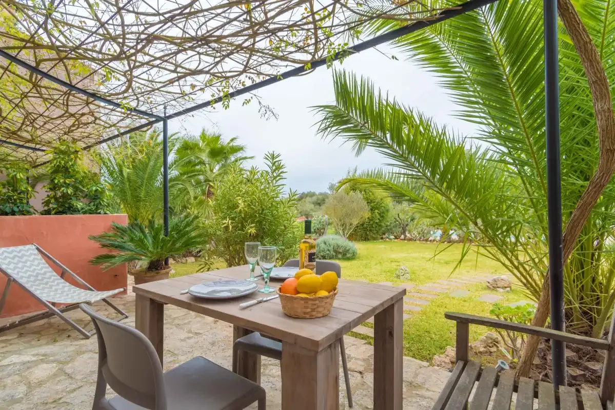 Un patio de jardín con una mesa de comedor de madera bajo una pérgola frondosa.