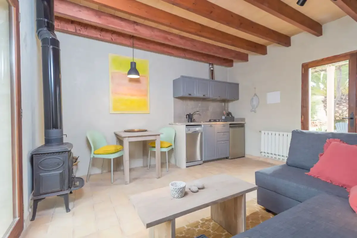 Una luminosa sala de estar y comedor tiene una mesa, una cocina compacta y asientos grises.