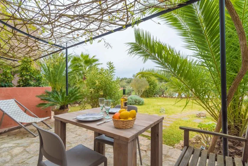 Un comedor al aire libre está bajo una pérgola frondosa junto a un jardín.