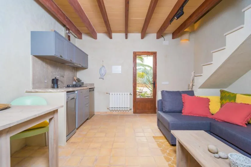 Sala de estar con una cocina compacta, una zona de asientos y vigas vistas en el techo.