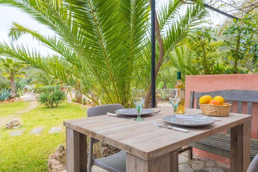 Una mesa de comedor al aire libre está junto a un jardín con palmeras.