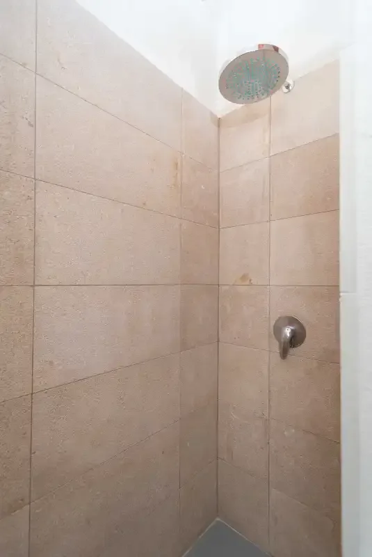 Una ducha alicatada con un cabezal redondo en lo alto y un control en la pared.