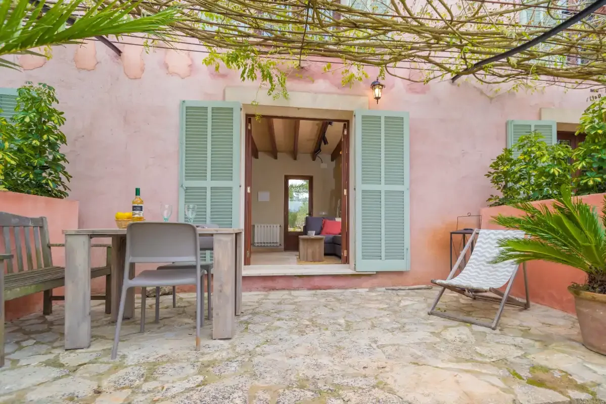 Un patio pavimentado con asientos al aire libre da a una puerta abierta en una pared exterior rosa.