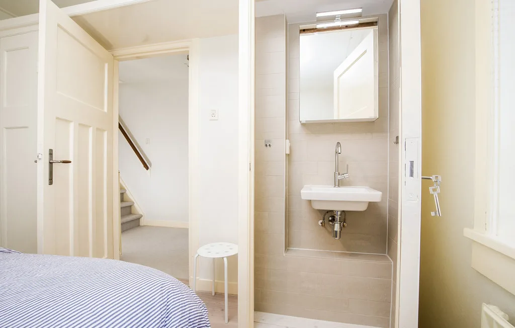 Un dormitorio da a un baño compacto con lavabo y espejo.