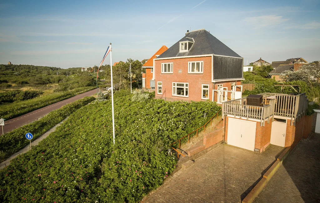 Una casa de ladrillo rojo está junto a una carretera, rodeada de campos verdes y jardines.
