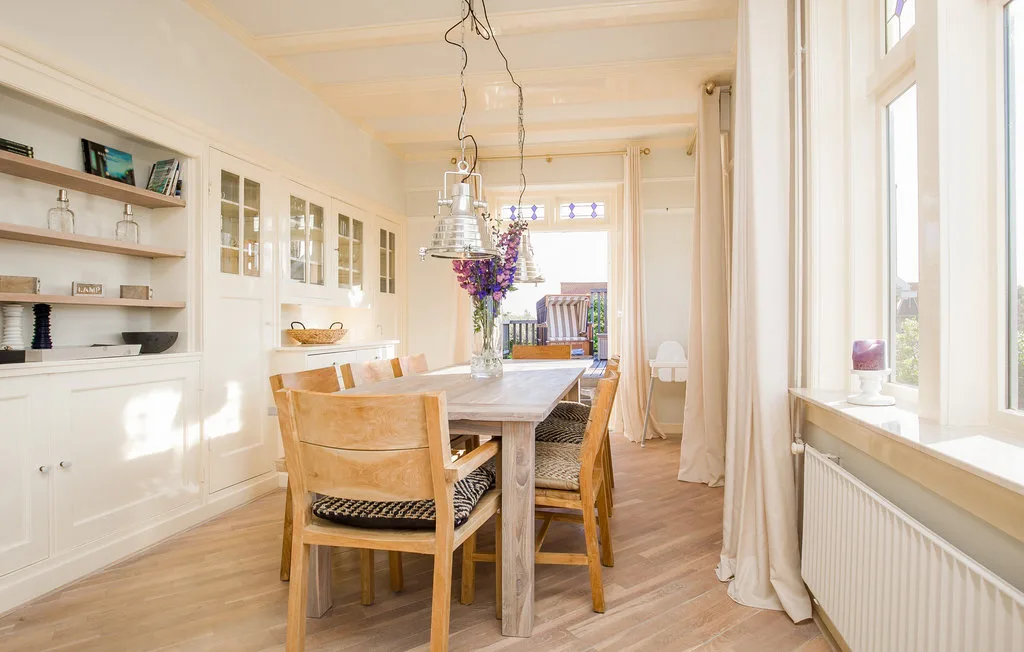 Un comedor luminoso con una mesa de madera, sillas y grandes ventanas.